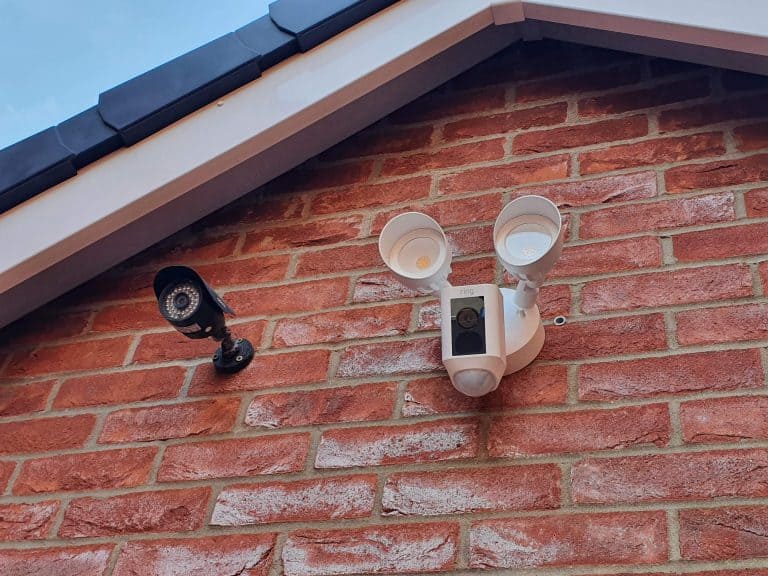 A second gen Ring Floodlight Cam Plus mounted next to a traditional CCTV camera