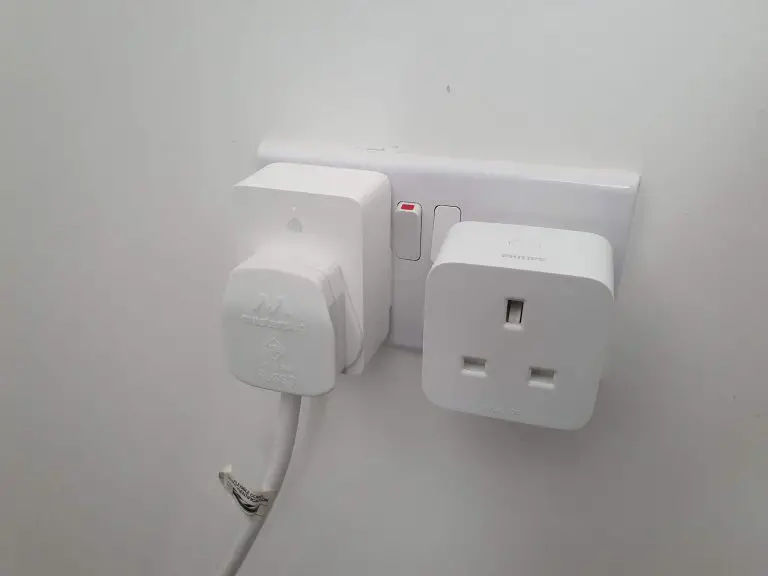 Two smart plugs a TP Link Kasa and Philips Hue one side by side in a UK wall socket